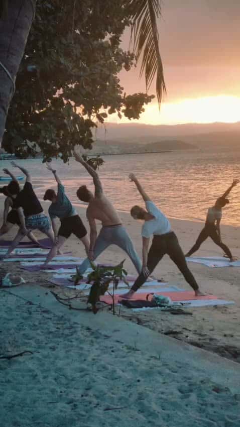 Group yoga class in a side-angle pose at sunset on Plai Leam Beach, Koh Samui