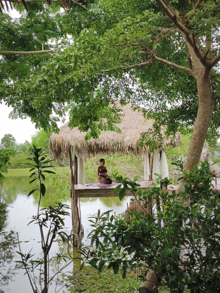 Meditation in a thatched sala over a tranquil pond, surrounded by lush greenery in Koh Samui